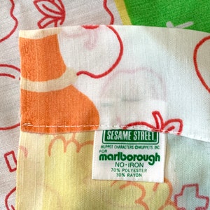 May include: A green fabric label with the text "Sesame Street" and "Marlborough" in white. The label also includes the text "Muppet Characters Muppets, Inc." and "No-Iron 70% Polyester 30% Rayon".