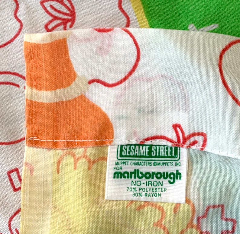 May include: A green fabric label with the text "Sesame Street" and "Marlborough" in white. The label also includes the text "Muppet Characters Muppets, Inc." and "No-Iron 70% Polyester 30% Rayon".