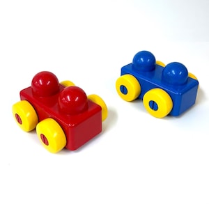 Op de afbeelding: Twee kleurrijke speelgoedauto's. Eén is rood met gele wielen, de andere is blauw met gele wielen. Elke auto heeft twee afgeronde vormen bovenop. Het speelgoed is ontworpen voor kinderen.