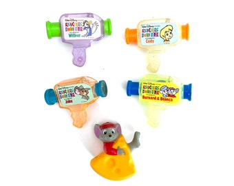 May include: Set of five plastic toys featuring characters from the Disney movie The Rescuers Down Under. The toys are shaped like movie cameras and feature different characters from the movie, including Wilbur, Cody, Jake, Bernard, and Bianca. The set also includes a small plastic figure of a mouse holding a piece of cheese.