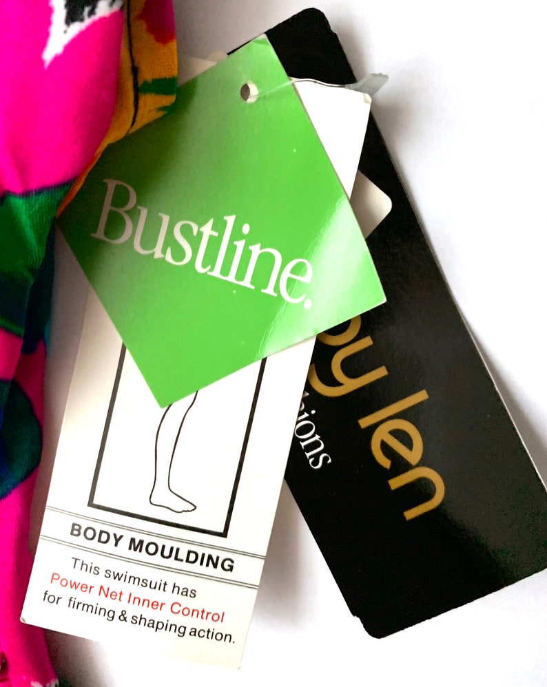 May include: A green and white tag with the text "Bustline." and the text "BODY MOULDING This swimsuit has Power Net Inner Control for firming & shaping action."  A black tag with gold text reads "py len Sions".