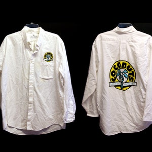 May include: White long-sleeve button-down shirt with a yellow and blue logo on the left chest and a larger version of the logo on the back. The logo says "Coconuts Music & Movies".