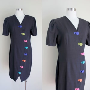 May include: A black short-sleeved dress with a V-neckline and a diagonal row of colorful buttons down the front.