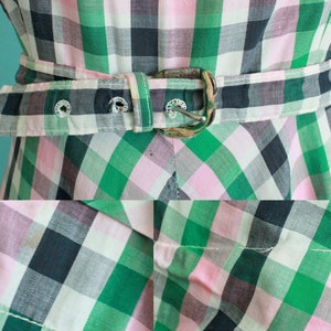 May include: A green, pink, and black plaid dress with a brown belt. The dress has a fitted bodice and a full skirt.