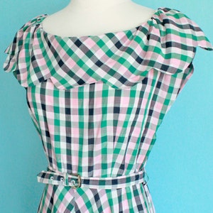 May include: A green, pink, and black gingham dress with a ruffled neckline and a belt. The dress has a zipper on the side.