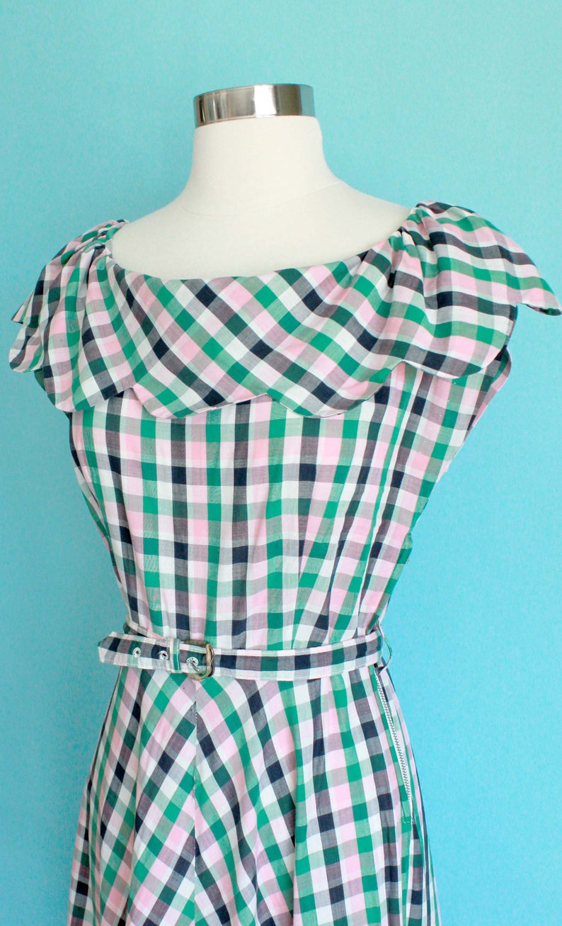 May include: A green, pink, and black gingham dress with a ruffled neckline and a belt. The dress has a zipper on the side.