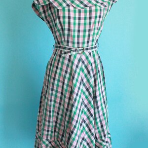 May include: A green, pink, and black gingham dress with a ruffled neckline and a matching belt. The dress has a full skirt and a scalloped hem.