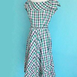 May include: A green, pink, and white gingham dress with a ruffled neckline and a matching belt. The dress has a fitted bodice and a full skirt.