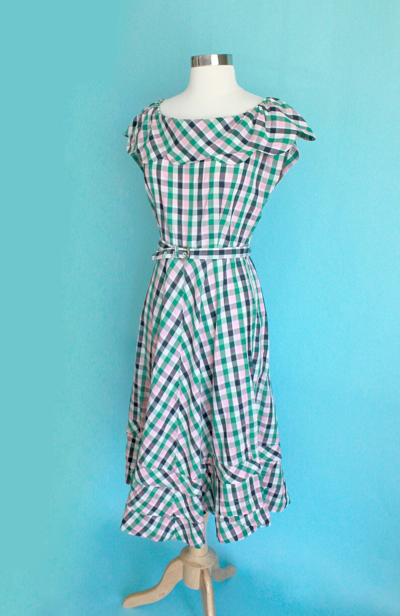 May include: A green, pink, and white gingham dress with a ruffled neckline and a matching belt. The dress has a fitted bodice and a full skirt.