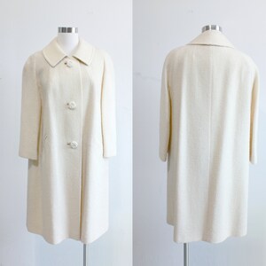 Vintage 1960s coat in a classic cream/ivory shade featuring a wide collar, swing coat fit, inset pockets and beautiful rose carved buttons.