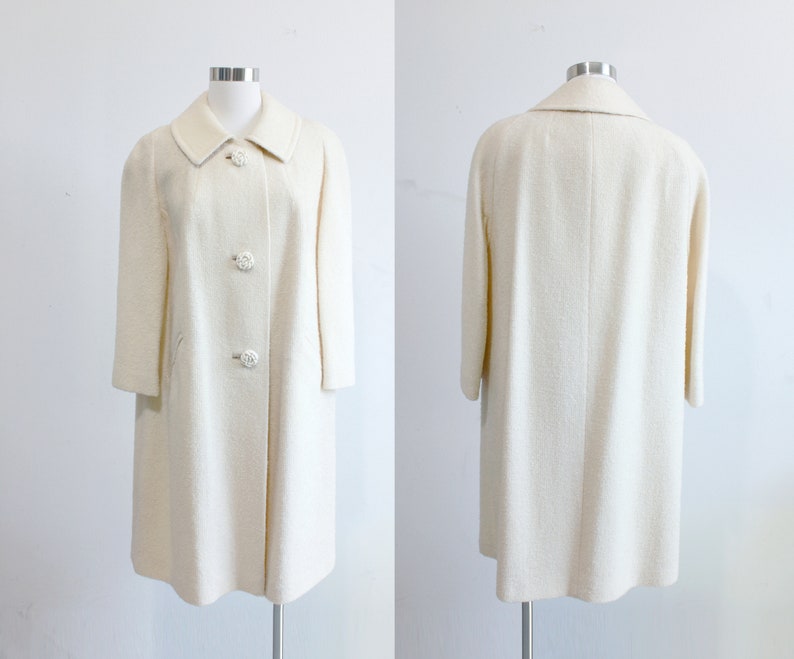 Vintage 1960s coat in a classic cream/ivory shade featuring a wide collar, swing coat fit, inset pockets and beautiful rose carved buttons.