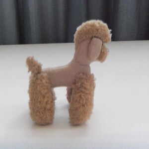 May include: A small, beige plush toy poodle with a fluffy tail and legs. The toy is made of soft, fuzzy fabric and has a realistic poodle shape.