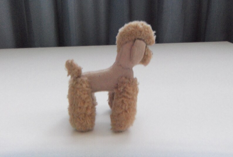 May include: A small, beige plush toy poodle with a fluffy tail and legs. The toy is made of soft, fuzzy fabric and has a realistic poodle shape.