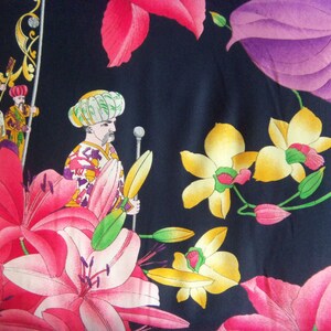 May include: A dark blue fabric with a colorful floral pattern. The pattern includes pink, yellow, and purple flowers, as well as three figures in traditional clothing.