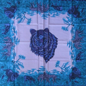 Pode incluir: Um lenço de seda branco com uma estampa de tigre azul e preto no centro. A borda do lenço apresenta um padrão repetido de zebras azuis e pretas e folhagem.
