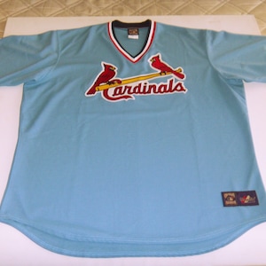 May include: A light blue baseball jersey with red cardinals and a baseball bat on the front. The jersey has the word "Cardinals" in red lettering on the front.