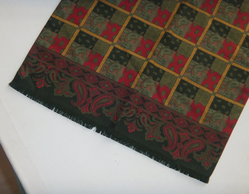 May include: A green and red paisley patterned scarf with a fringed edge.
