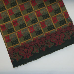 May include: A green, red, and gold patterned scarf with a paisley border. The scarf has a fringed edge.