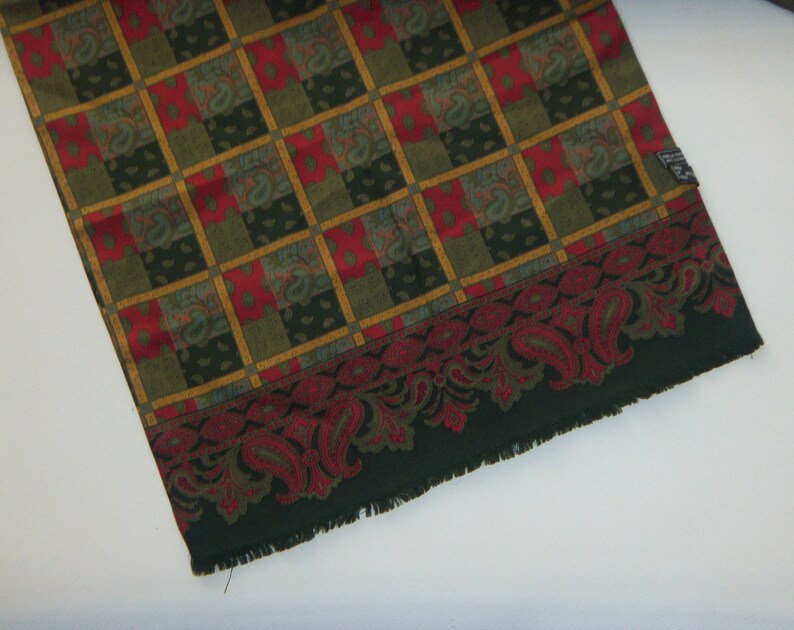 May include: A green, red, and gold patterned scarf with a paisley border. The scarf has a fringed edge.