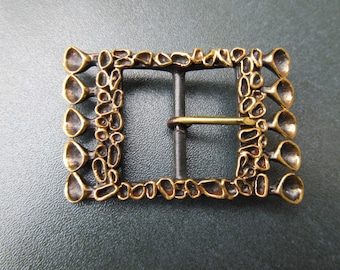 Peut inclure: Une boucle de ceinture en métal doré avec un design texturé et organique. La boucle a une forme rectangulaire avec une barre en métal noir lisse pour la fixation.