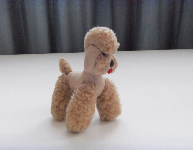May include: A small, beige plush toy poodle with a red nose and a curly, fluffy coat.