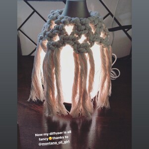 Op de afbeelding: Een witte etherische olieverdamper met een gehaakte macram&eacute;-hoes. De diffuser is verlicht en gloeit. De tekst "Now my diffuser is all fancy thanks to @montana_oil_girl" is zichtbaar onder de diffuser.