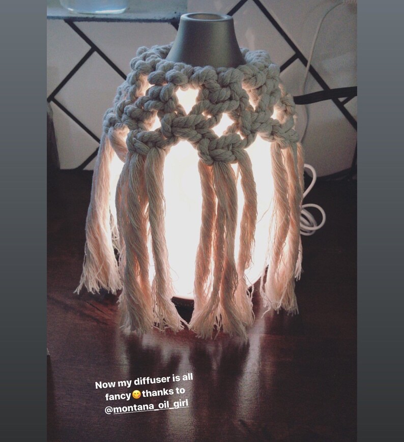 Op de afbeelding: Een witte etherische olieverdamper met een gehaakte macram&eacute;-hoes. De diffuser is verlicht en gloeit. De tekst "Now my diffuser is all fancy thanks to @montana_oil_girl" is zichtbaar onder de diffuser.