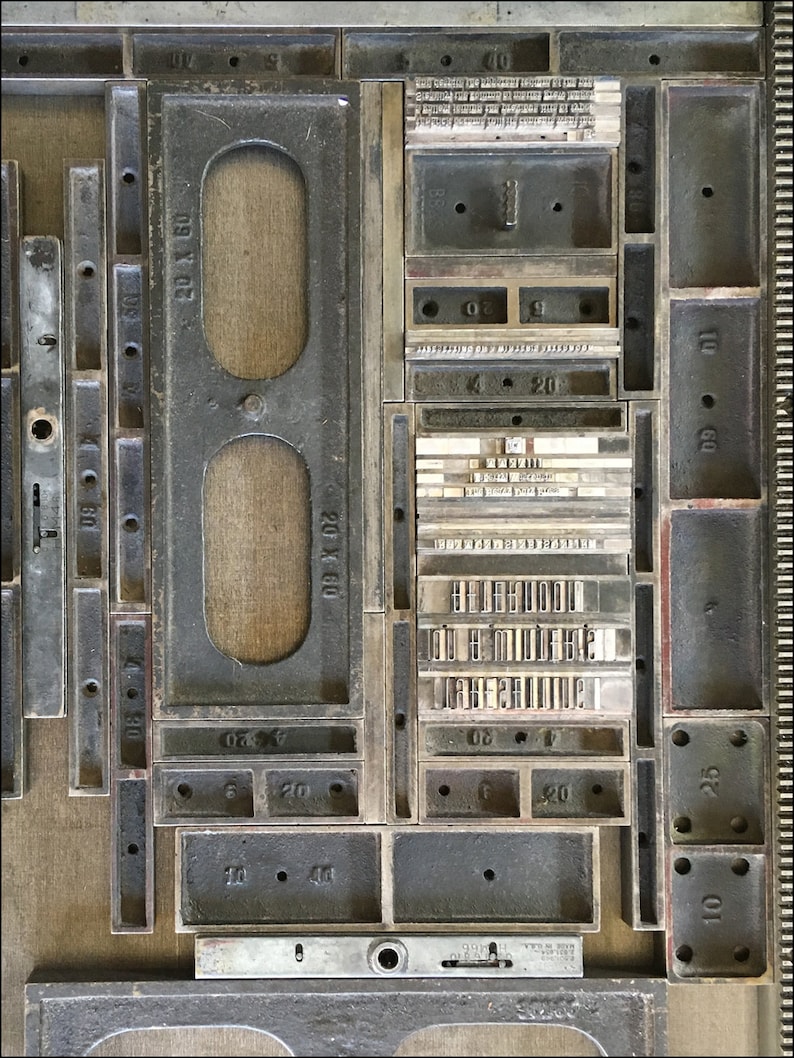 May include: A close-up of a metal printing press with various sized metal trays. The trays are labeled with numbers and have small holes in them. The trays are arranged in a grid pattern.