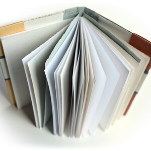 May include: A handmade book with a brown, tan, and blue patterned cover. The book is open, revealing blank white pages.