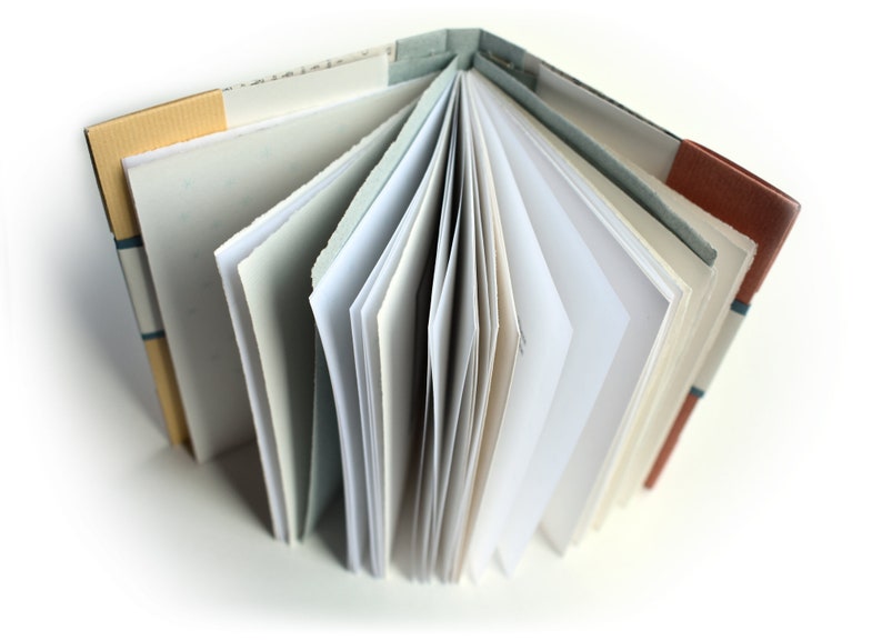 May include: A handmade book with a brown, tan, and blue patterned cover. The book is open, revealing blank white pages.