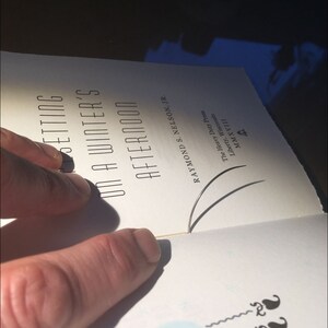 May include: A close-up of a book titled "Setting on a Winter's Afternoon" by Raymond S. Nelson, Jr. The book is open to a page with a blue circle and two black squiggly lines.