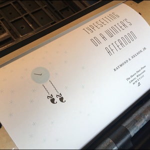 May include: A white book cover with the title "Typesetting on a Winter's Afternoon" by Raymond S. Nelson, Jr. The cover features a simple illustration of a clock with two black hearts hanging from it. The book is published by The Heavy Duty Press in Liberty, Wisconsin.