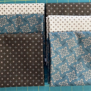 May include: A collection of folded fabric squares featuring three distinct patterns. Two squares display a dark brown background with a white and light blue dot and cross motif. Two squares feature a teal background with a light pink floral-like knot pattern. One square has a white background with a brown and light blue dot and cross pattern.