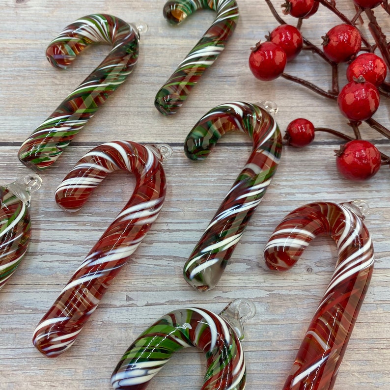 May include: Six glass candy cane ornaments with red, white, and green swirl patterns. The ornaments are arranged on a light wood surface.