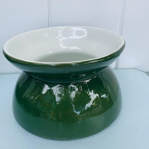 Puede incluir: Un macetero de cerámica verde con interior blanco. El macetero tiene una base ancha y redonda y una abertura estrecha.