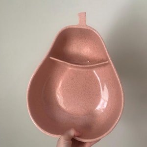 Puede incluir: Un bol de servir de color rosa en forma de pera con dos secciones. El bol está hecho de un material texturizado y tiene un acabado brillante.
