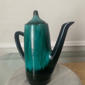 May include: A green and black ceramic teapot with a spout and handle. The teapot has a glaze that creates a marbled effect.