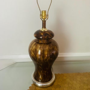 Könnte beinhalten: Eine braune und goldene Tischlampe mit einem Sockel aus Schildpattmuster und einem goldenen Lampenschirm.