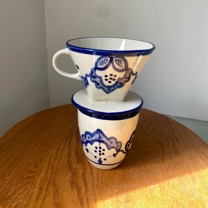 May include: A white ceramic mug with a black handle and the text "But First, Coffee" in a black, bold font. The mug is on a white surface. The mug is approximately 4 inches tall.