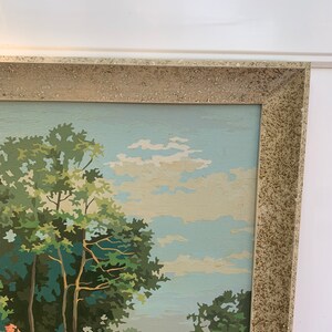 Puede incluir: Una pintura enmarcada de una escena de paisaje con un puente de piedra, &aacute;rboles y un cielo azul con nubes blancas.