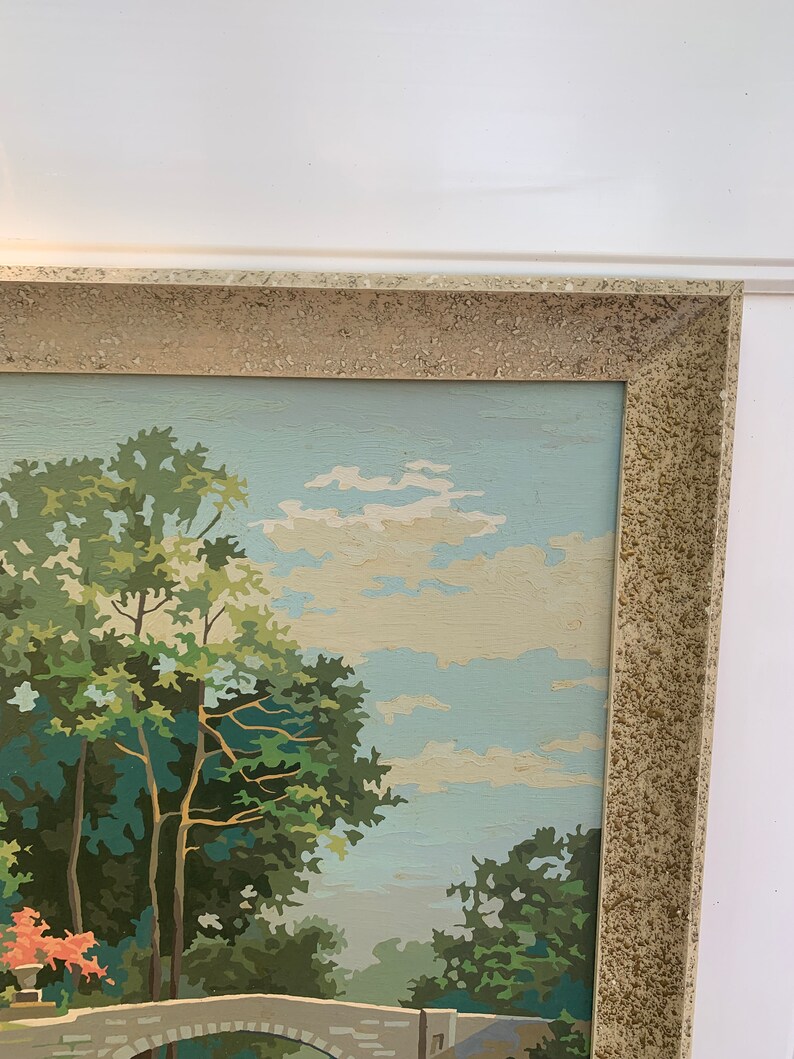Puede incluir: Una pintura enmarcada de una escena de paisaje con un puente de piedra, &aacute;rboles y un cielo azul con nubes blancas.