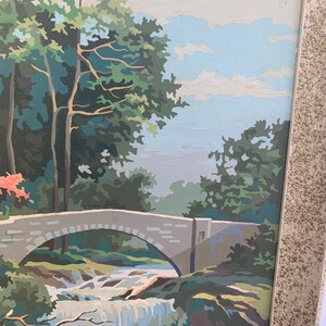Puede incluir: Una pintura de un puente de piedra sobre una cascada que cae en un entorno boscoso. El cielo es azul con nubes blancas. Los &aacute;rboles son verdes y el agua es azul y blanca.