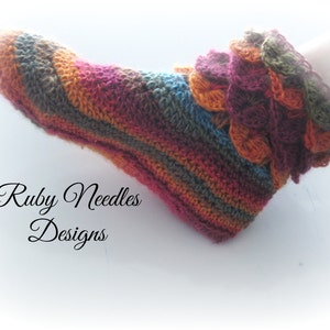 May include: Multicolored crochet sock with a ruffled top. The sock is made with a variety of shades of brown, orange, red, and blue yarn. The text "Ruby Needles Designs" is visible in the image.