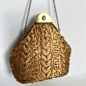 Puede incluir: Un bolso de noche de cuentas doradas con una correa de cadena y un cierre dorado. El bolso está decorado con un patrón de cuentas.