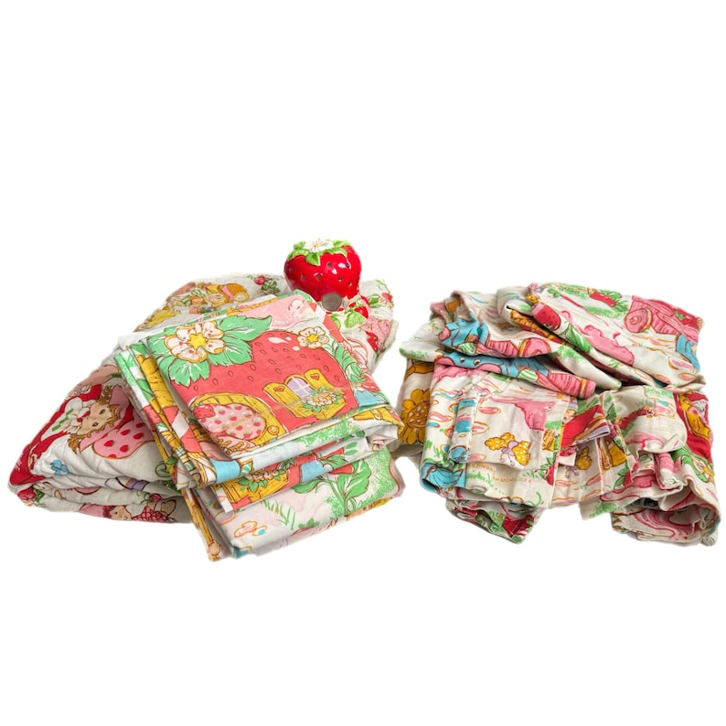 May include: A set of vintage Strawberry Shortcake bedding featuring a pink, red, and green floral pattern with strawberries and characters. The bedding includes a flat sheet, fitted sheet, and pillowcases.