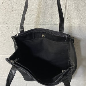 May include: Black leather tote bag with two zipped compartments and a single top handle.