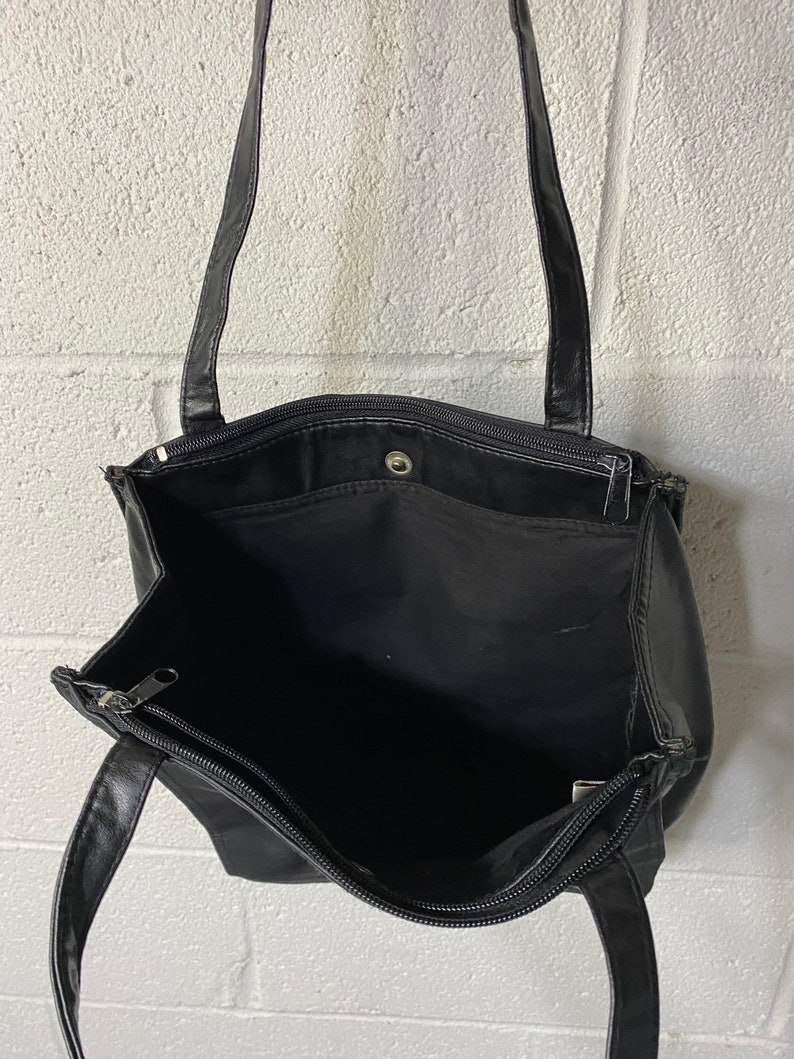 May include: Black leather tote bag with two zipped compartments and a single top handle.