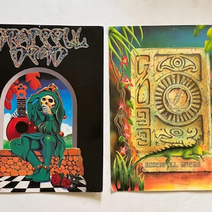 May include: Two vintage Grateful Dead album covers. One features a jester skeleton in green attire with a guitar, the band's name in colorful lettering above. The other shows a stone structure with a lizard and the text "ACCESS ALL AREAS".
