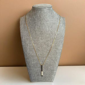 Può includere: Una collana con catena dorata e un ciondolo rettangolare bianco e nero.