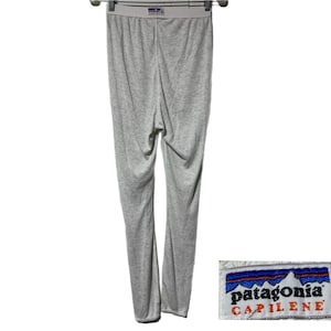 Può includere: Pantaloni intimo termico grigi Patagonia Capilene. I pantaloni hanno una cintura bianca con un logo Patagonia blu e bianco.